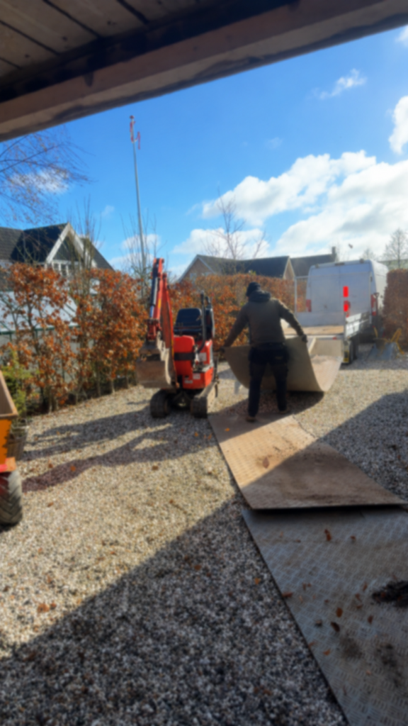 Flytning af stor stenplade med minigraver på grusareal